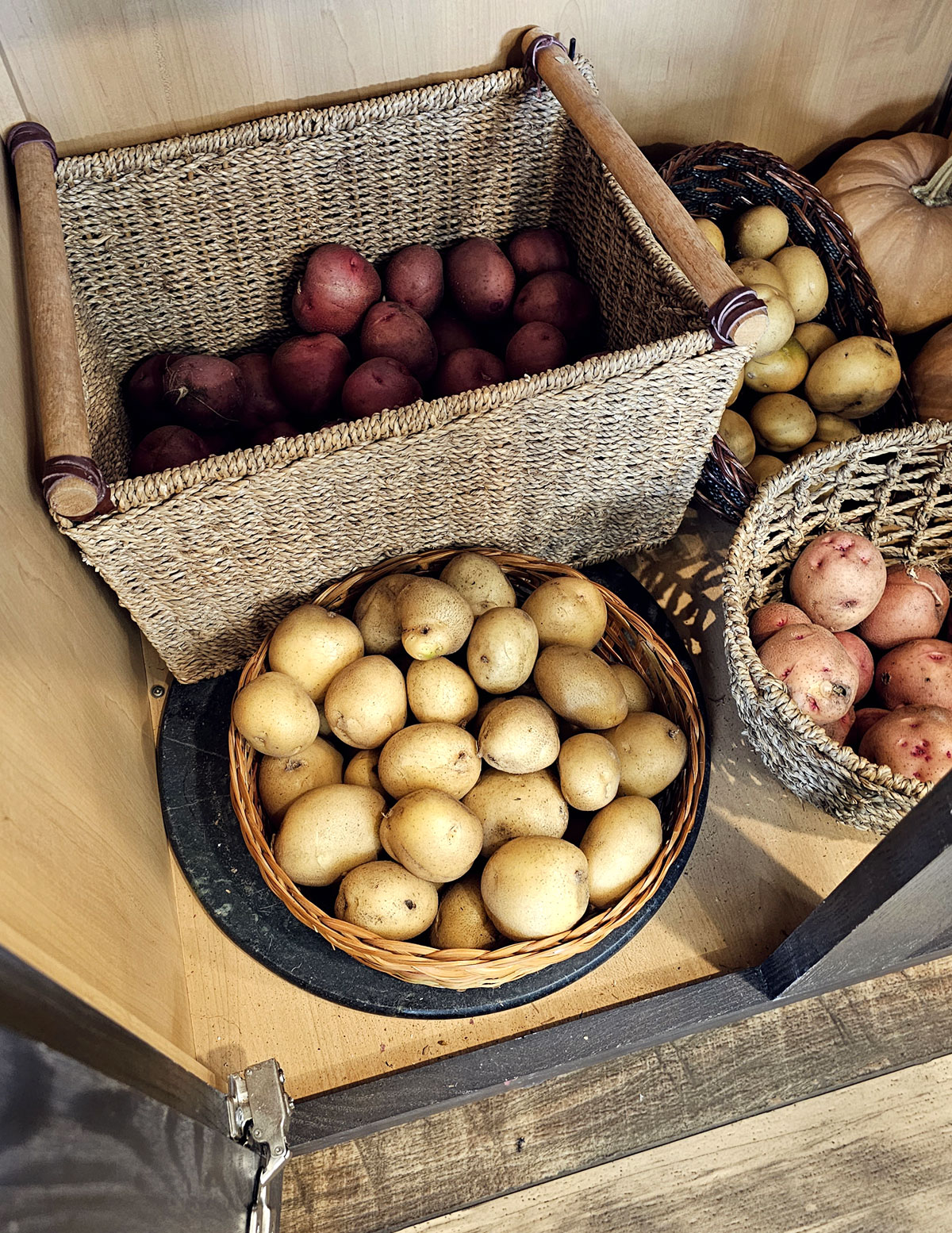 kitchen pantry with 3 baskets of potatoes and 2 squashes