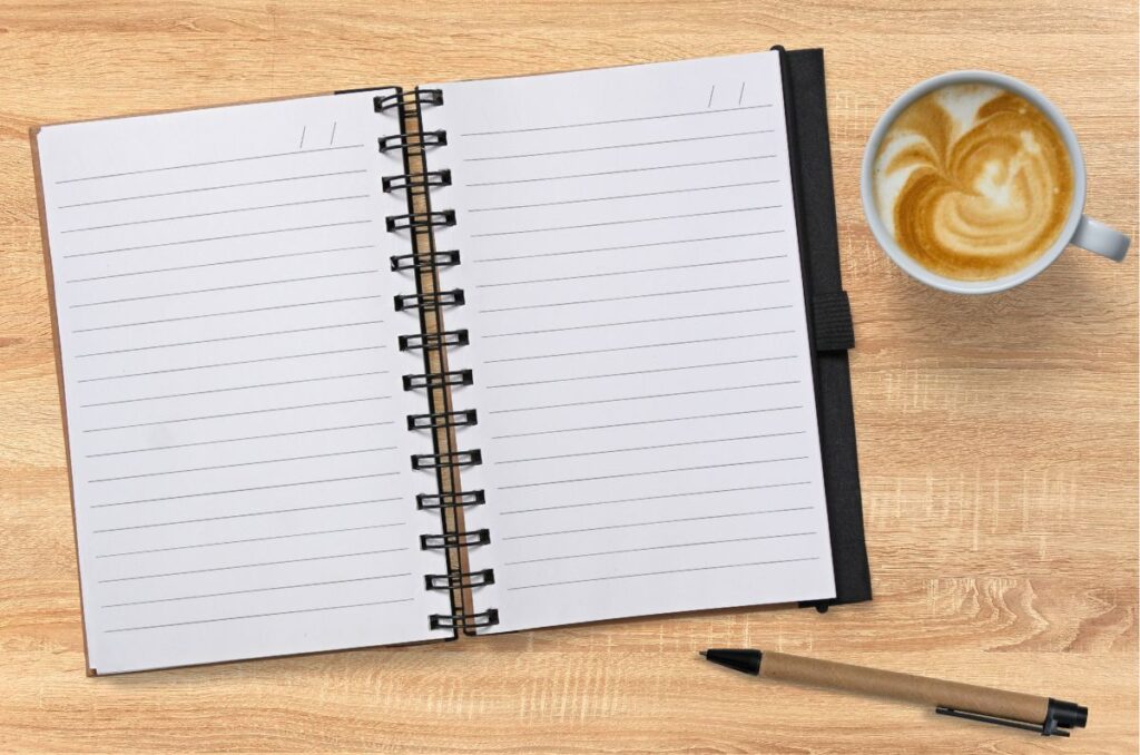 photo of a notebook, pen, and cup of coffee on a wood table top.