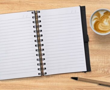 photo of a notebook, pen, and cup of coffee on a wood table top.