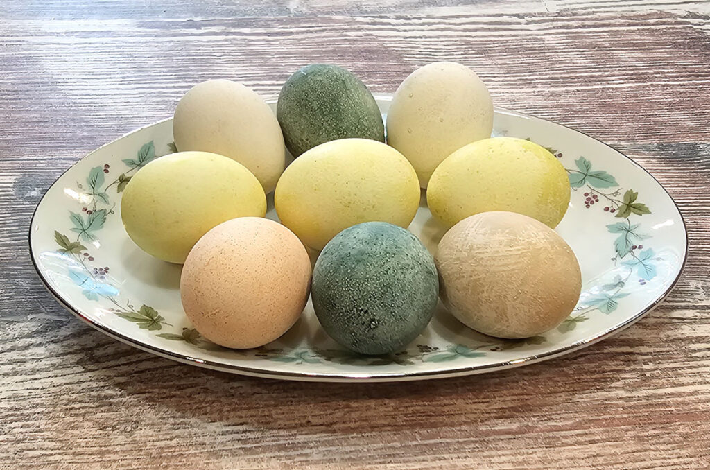 Photo of 9 Easter eggs dyed in pastel colors laying on a decorative plate on a table.