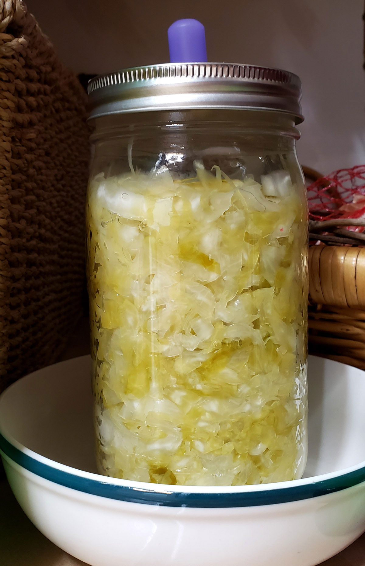 fermented cabbage in a mason jar sitting in a bowl in a pantry.