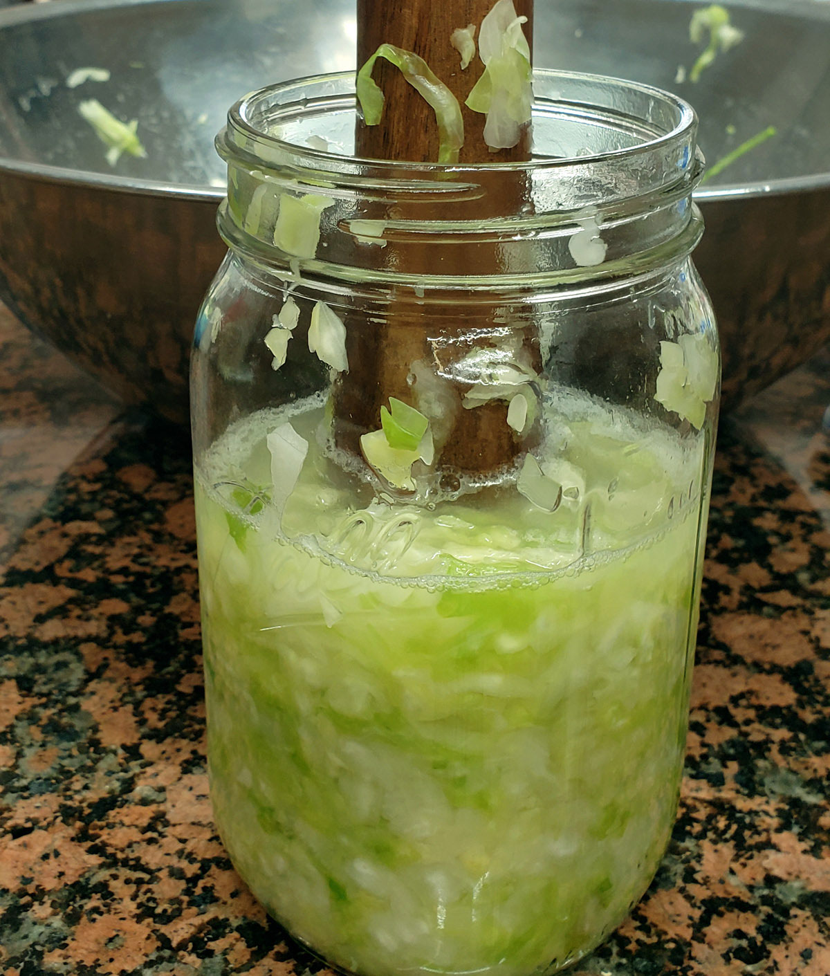 Wooden tool mashing cabbage in a quart mason jar