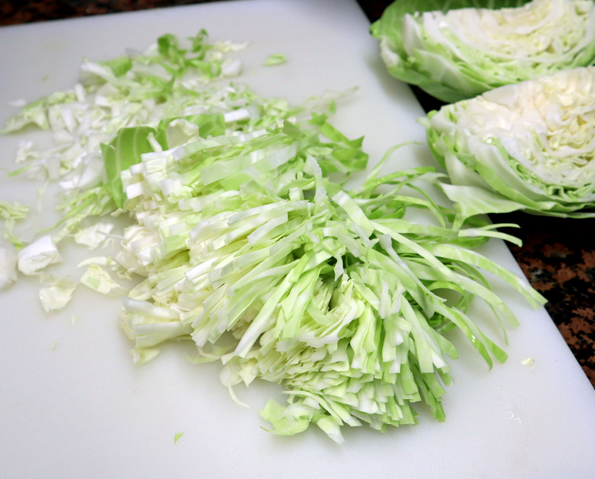 shredded cabbage leaves on a white cutting board.