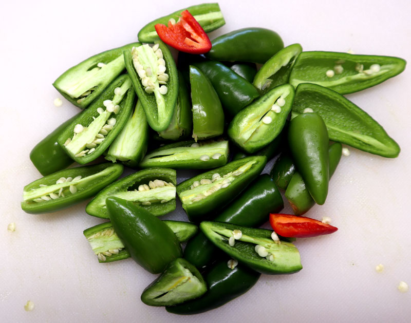 jalapeno peppers cut in half on a white cutting board