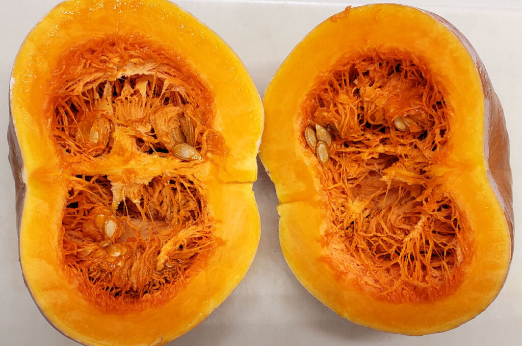 Seminole pumpkin cut in half on a white plastic cutting board.