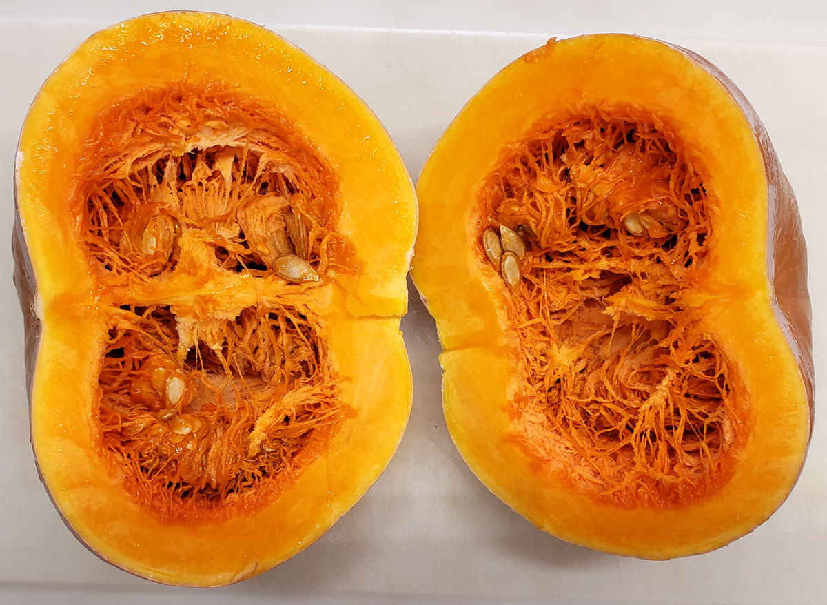 Seminole pumpkin cut in half on a white plastic cutting board.