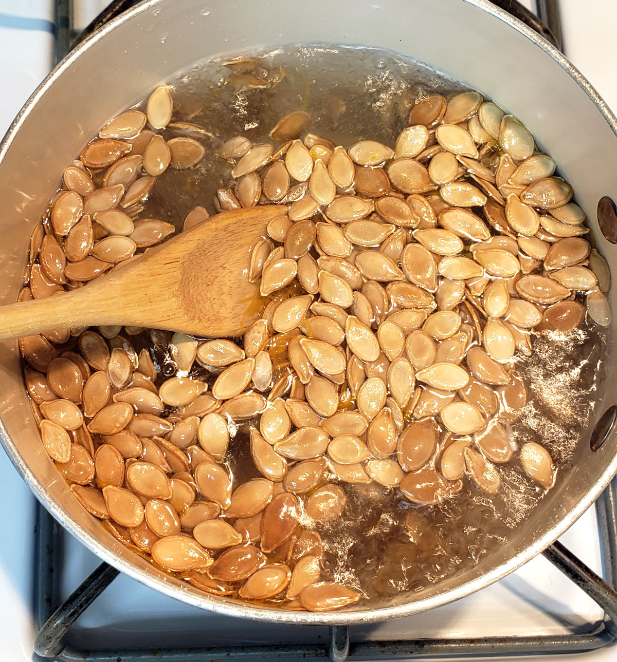 pumpkin seeds boiling in water in a pot with a wooden spoon stirring.