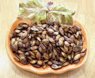 Pumpkin shaped bowl with roasted pumpkin seeds setting in it.