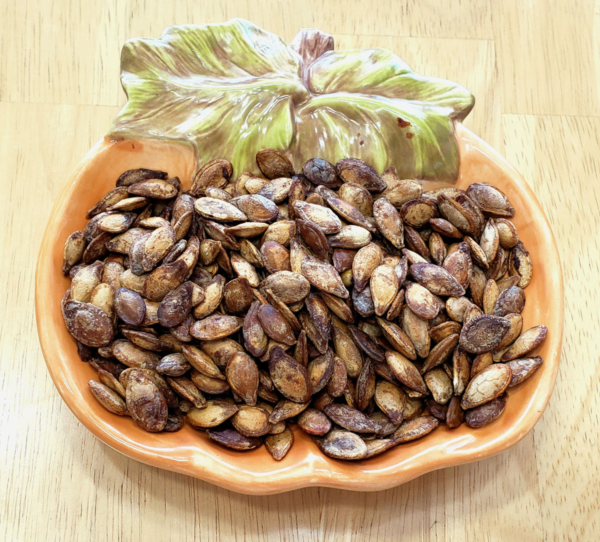 Pumpkin shaped bowl with roasted pumpkin seeds setting in it.