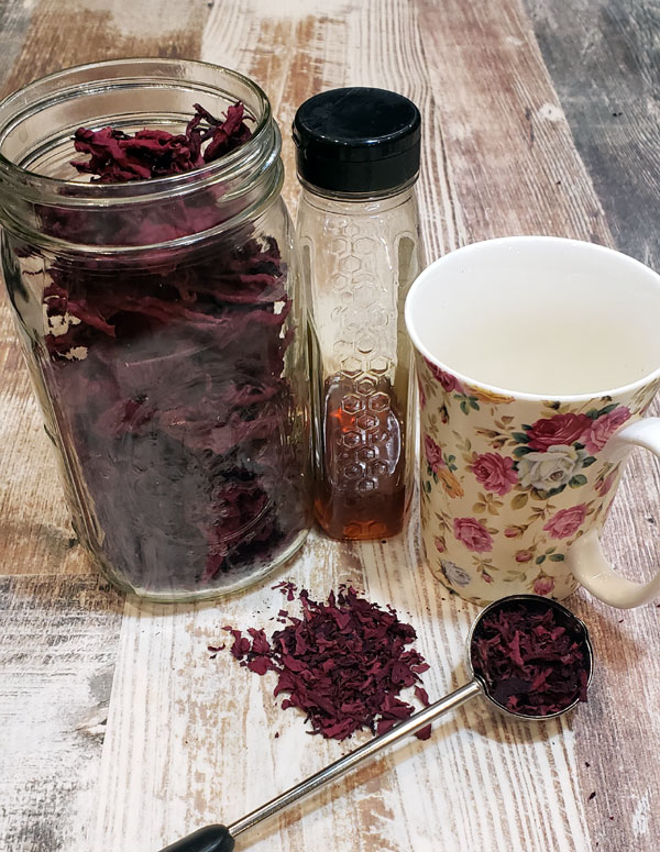 dried cranberry hibiscus leaves in a glass jar with tea cup, honey and tea strainer