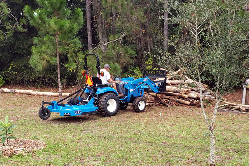 Mike using forks on the tractor to pick up long pine logs.