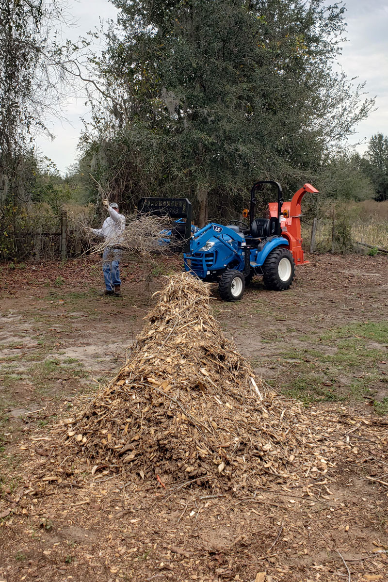 pile of wood chipped into mulch with a blue LS tractor and orange wood chipper in the backgfound.