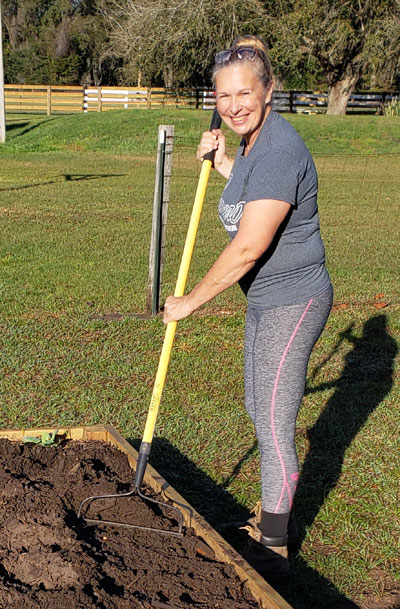 Alisa standing next to a raised garden bed with a rake in her hands.