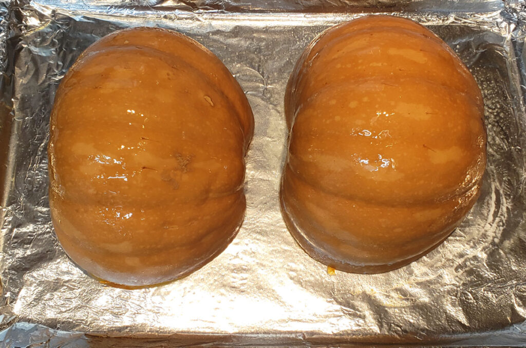 Seminole Pumpkin halves on an aluminum foil lined baking pan. The halves are cut side down and lightly oiled.