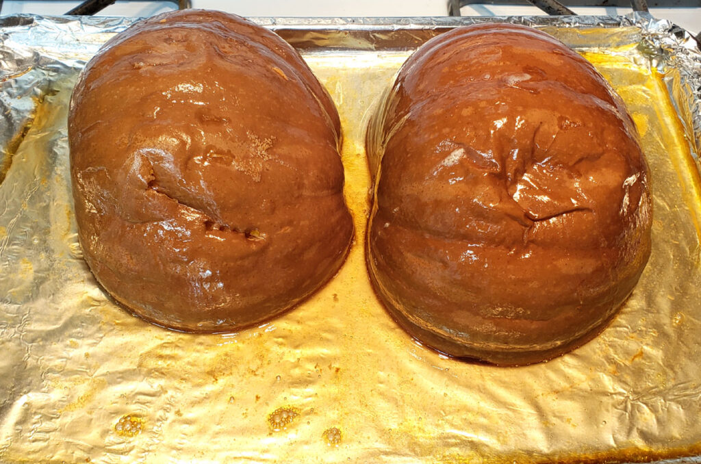 Baked Semminole Pumpkin halves on a baking sheet lined with aluminum foil. Juices from the pumpkin are laying in the bottom of the pan.