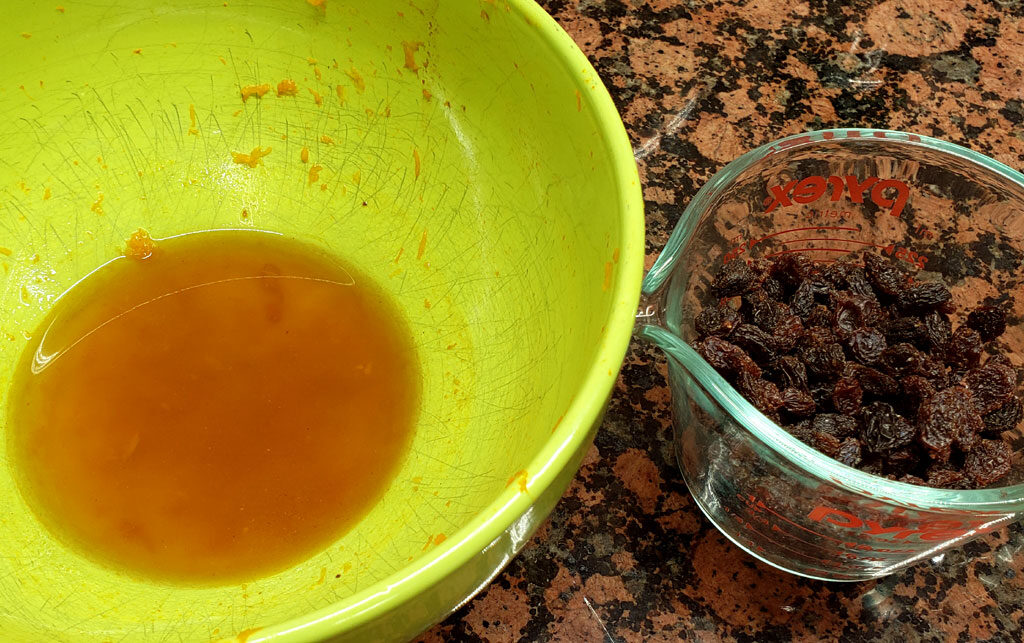 A large green bowl with pumpkin liquid in the bottom. Next to the bowl is a glass measuring cup with raisins inside.