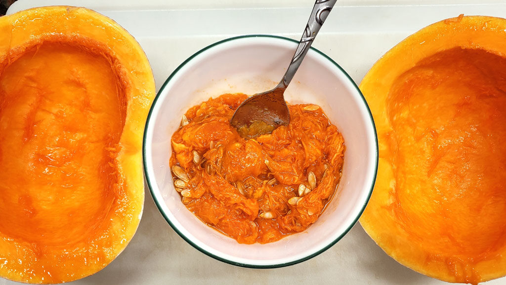 Pumpkin cut in half sitting on a cutting board with a bowl of seeds and pumpkin pulp between the halves.