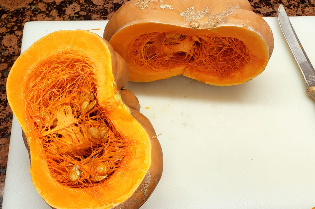 Pumpkin cut in half sitting on a cutting board.