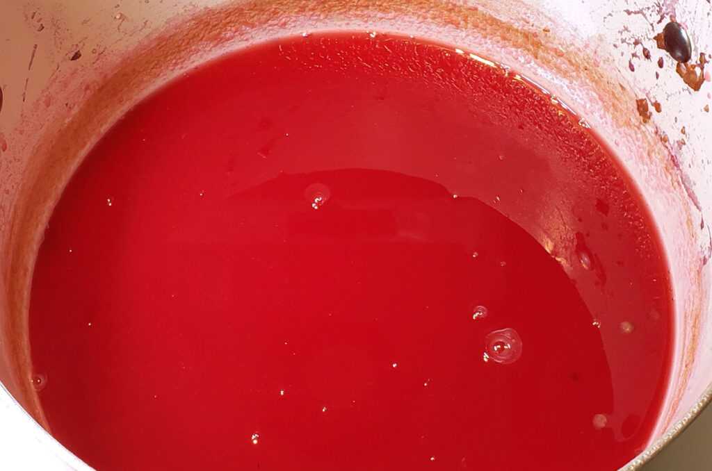 Bright reddish-pink beautyberry juice in a pot.