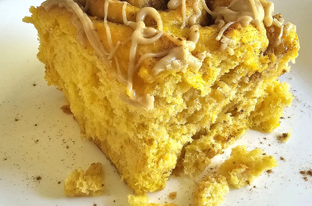 Close-up photo of a pumpkin cinnamon roll with caramel glaze on top. Roll is sitting on a white plate.