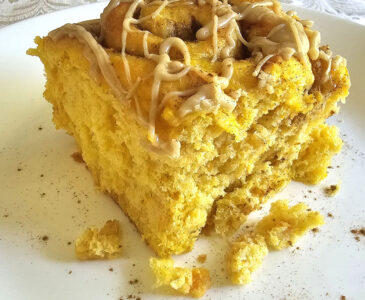 Close-up photo of a pumpkin cinnamon roll with caramel glaze on top. Roll is sitting on a white plate.