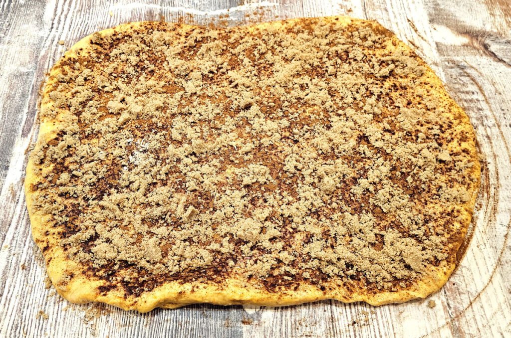 Pumpkin cinnamon roll dough rolled out on a table with butter, cinnamon, and brown sugar spread across the top.