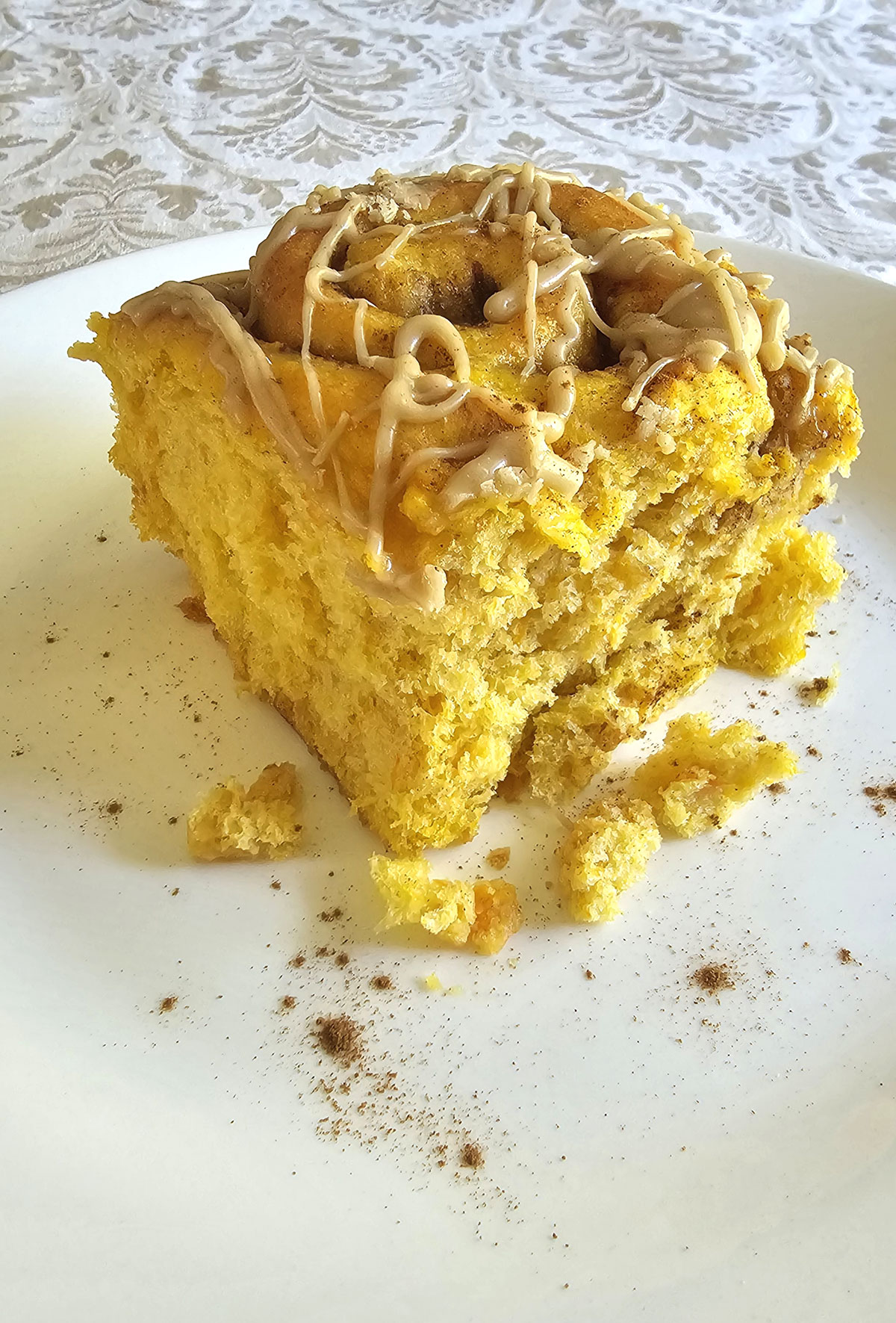 Pumpkin cinnamon roll with caramel glaze sitting on a white plate on a vintage white tablecloth.