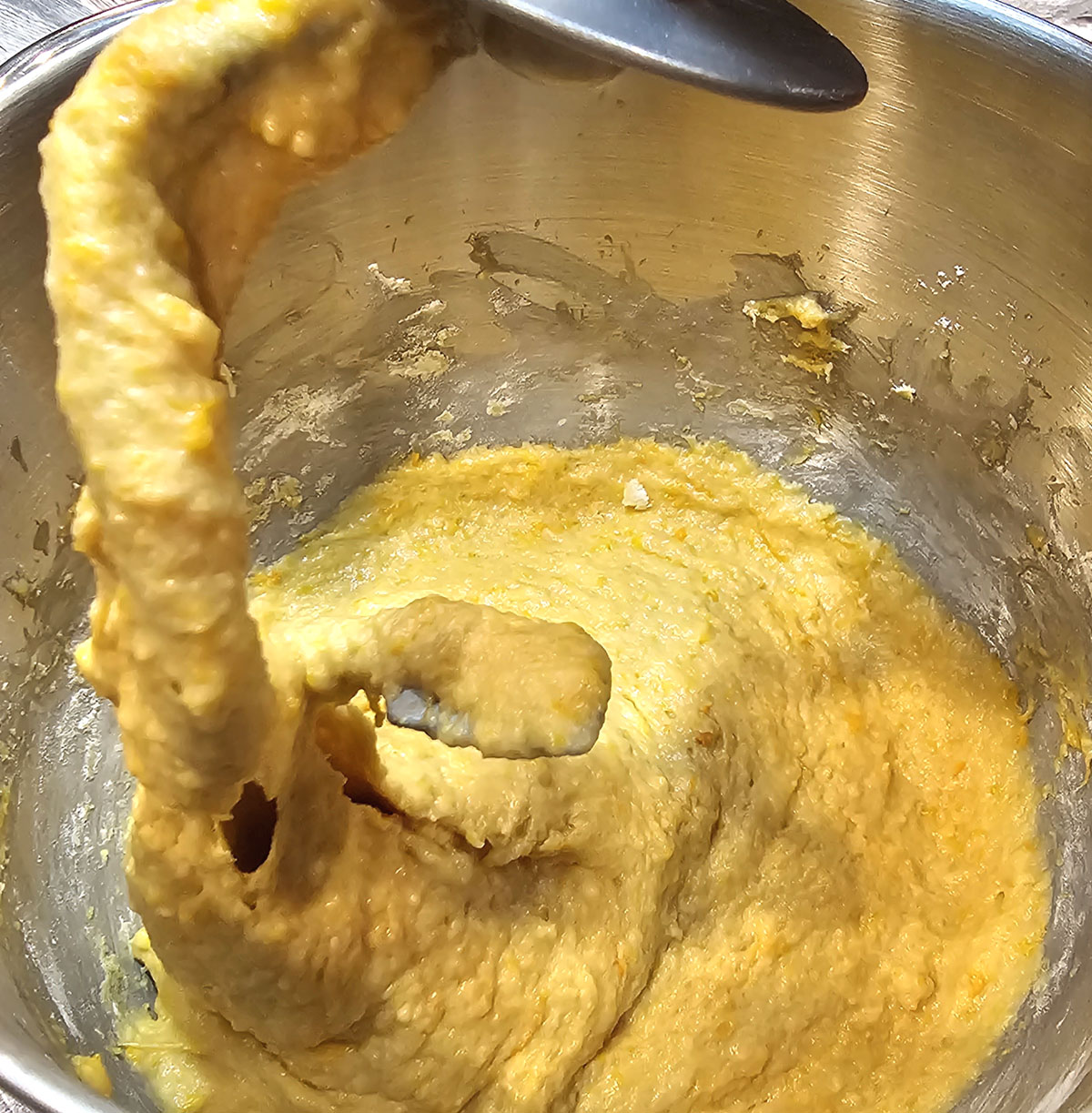 Dough hook on a stand mixer with pumpkin roll dough all over it.