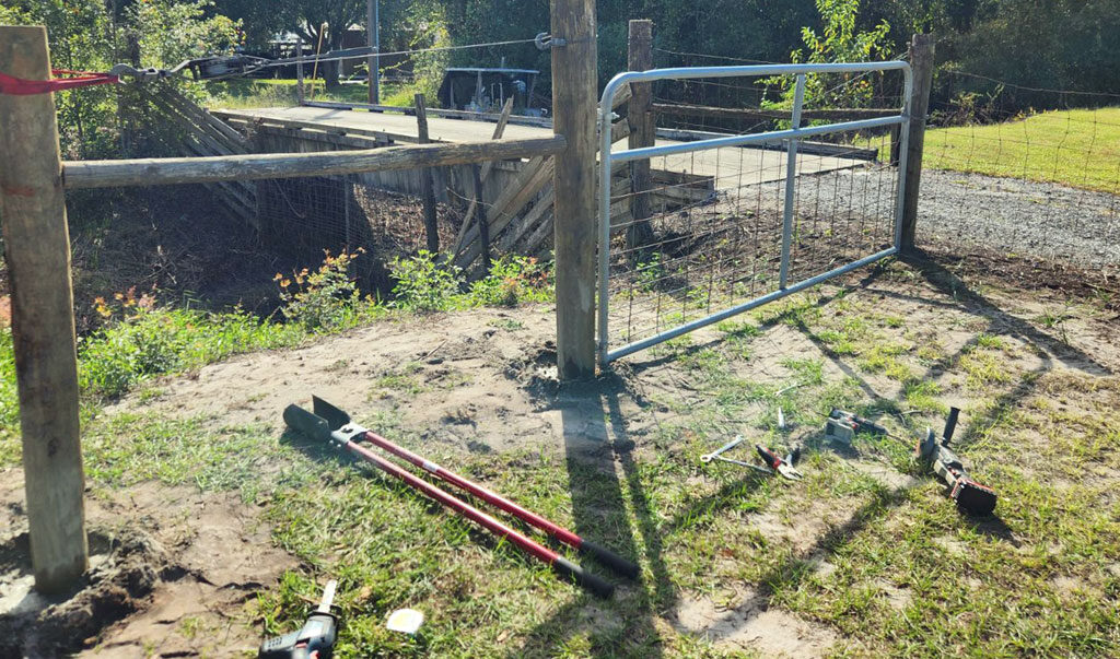 photo of tlls to install a fence post laying on the ground next to a newly-installed H-brace for fencing.