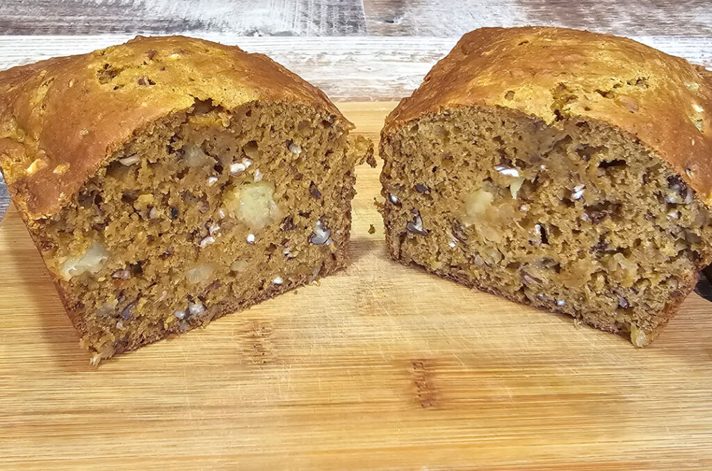 A loaf of sweet potato pineapple bread cut in half on a bamboo bread board.