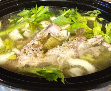 Crockpot filled with a turkey carcass, onions, carrots, celery, herbs and spices.