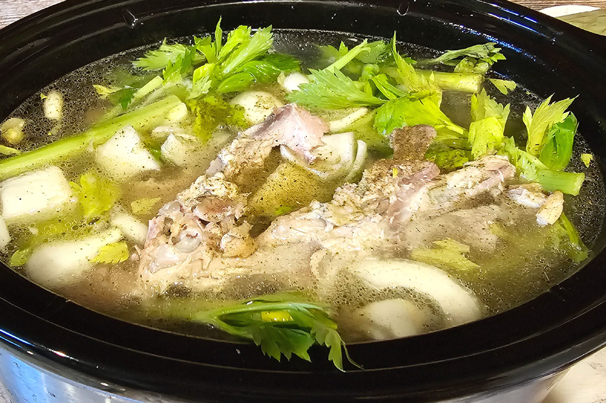 Crockpot filled with a turkey carcass, onions, carrots, celery, herbs and spices.