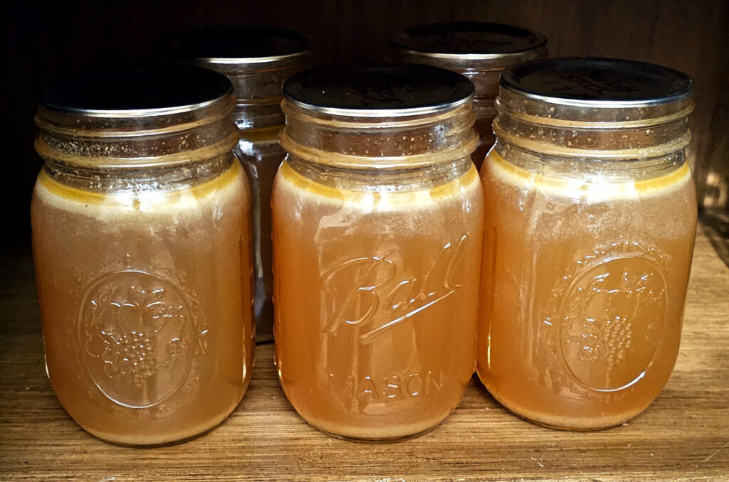 5 pint canning jars full of turkey broth sitting on a wood shelf.