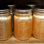 5 pint canning jars full of turkey broth sitting on a wood shelf.