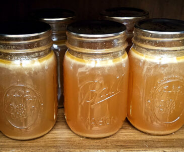 5 pint canning jars full of turkey broth sitting on a wood shelf.