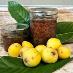 2 jars of loquat jam arranged with fresh fruit and leaves.