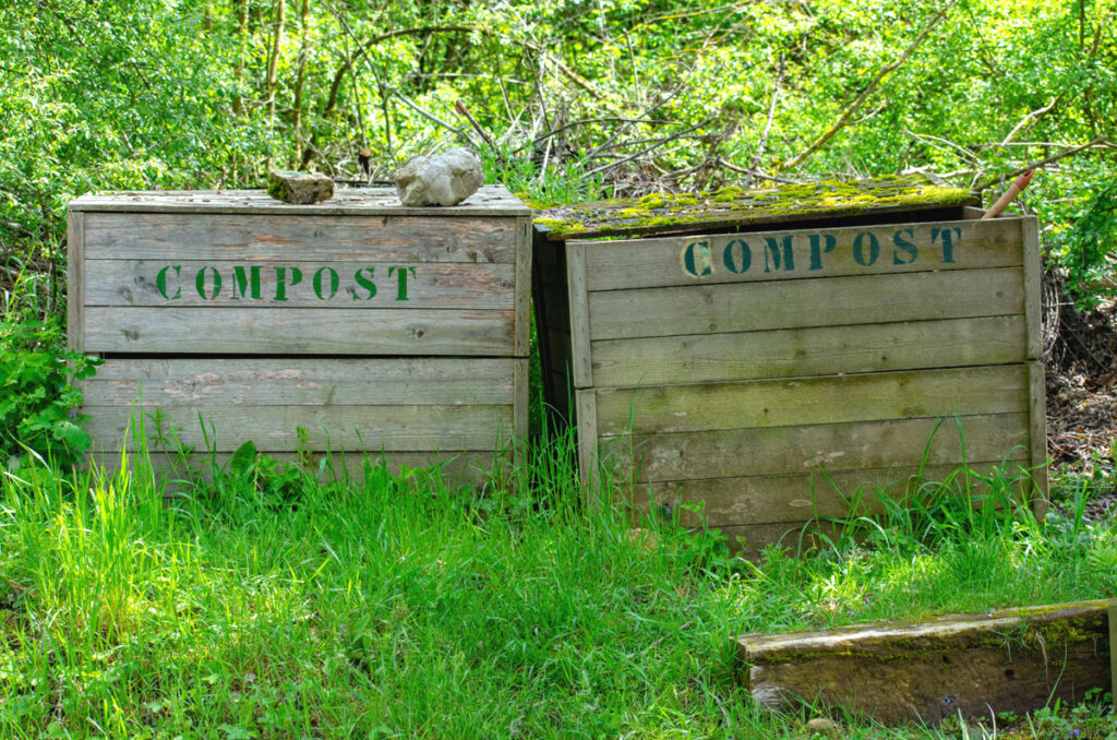 2 wooden compost bins setting next to/under a large tree in the shade.