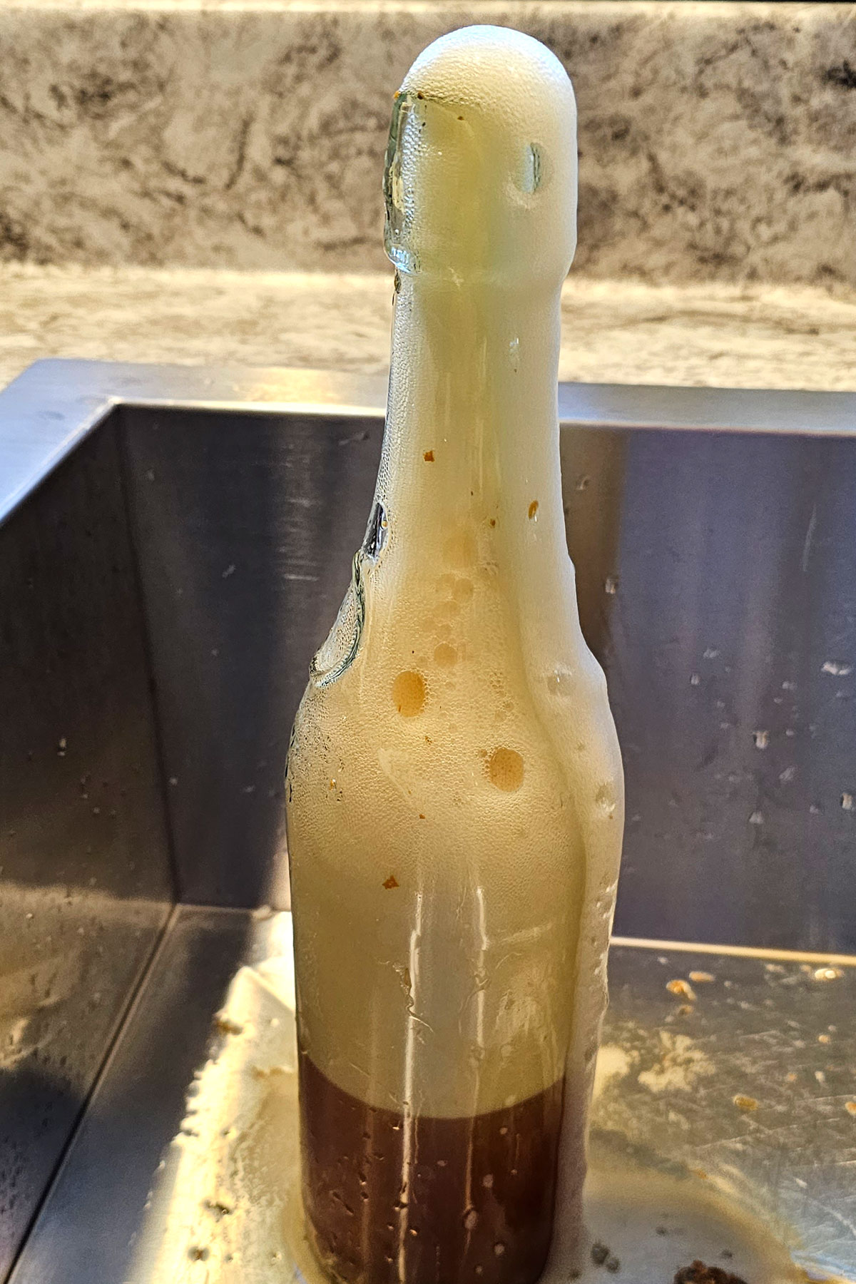 A glass bottle overflowing with foam from an overfermented kobucha.