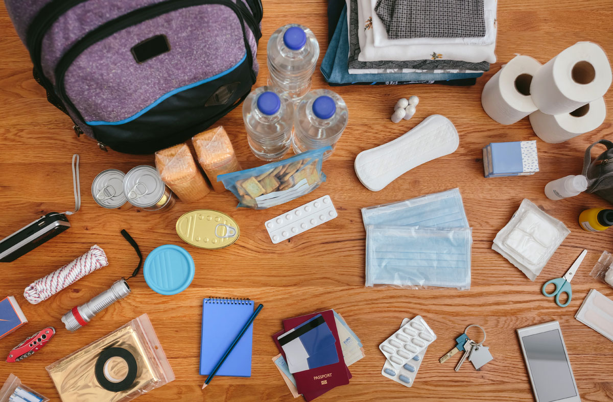 A display of first-aid and emergency supplies next to a backpack on a tabletop. Overhead view.