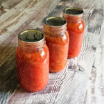 3 Quart jars of canned stewed tomatoes sitting on a countertop.