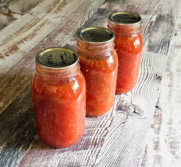 3 Quart jars of canned stewed tomatoes sitting on a countertop.