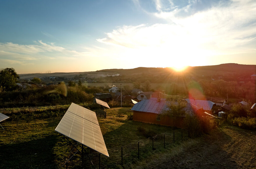 Homestead with solar panel array in the field nearby. Sun is setting.