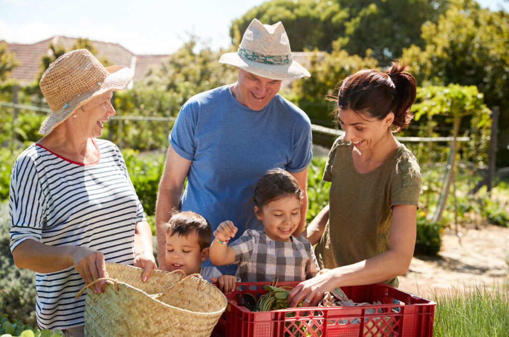 3 generations standing in a garden holding baskets of fresh picked produce.