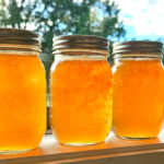 3 pint jars of maypop jelly sitting on a windowsill with the sunlight shining through the jars.