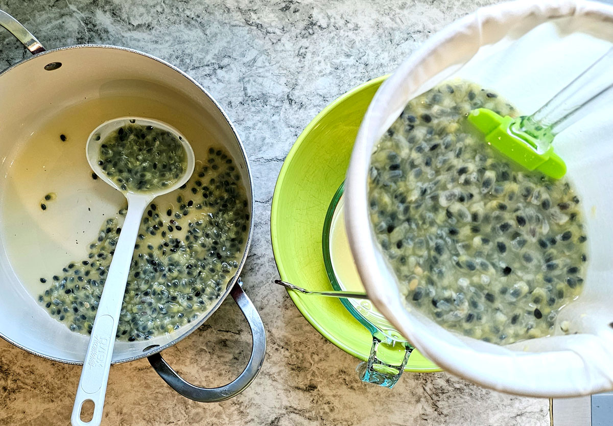 photo of a pot of maypop pulp next to a jelly strainer with pulp being strained, the juice dripping into a large bowl.