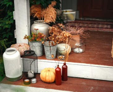 Photo fall decor on front porch steps includes pails of dried flowers, buckets, pumpkins and luminaries.