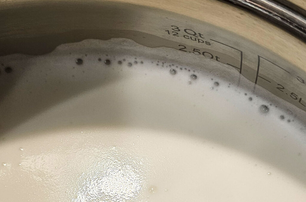 Milk foaming in a stainless steel pot, almost to 180 degrees Fahrenheit.