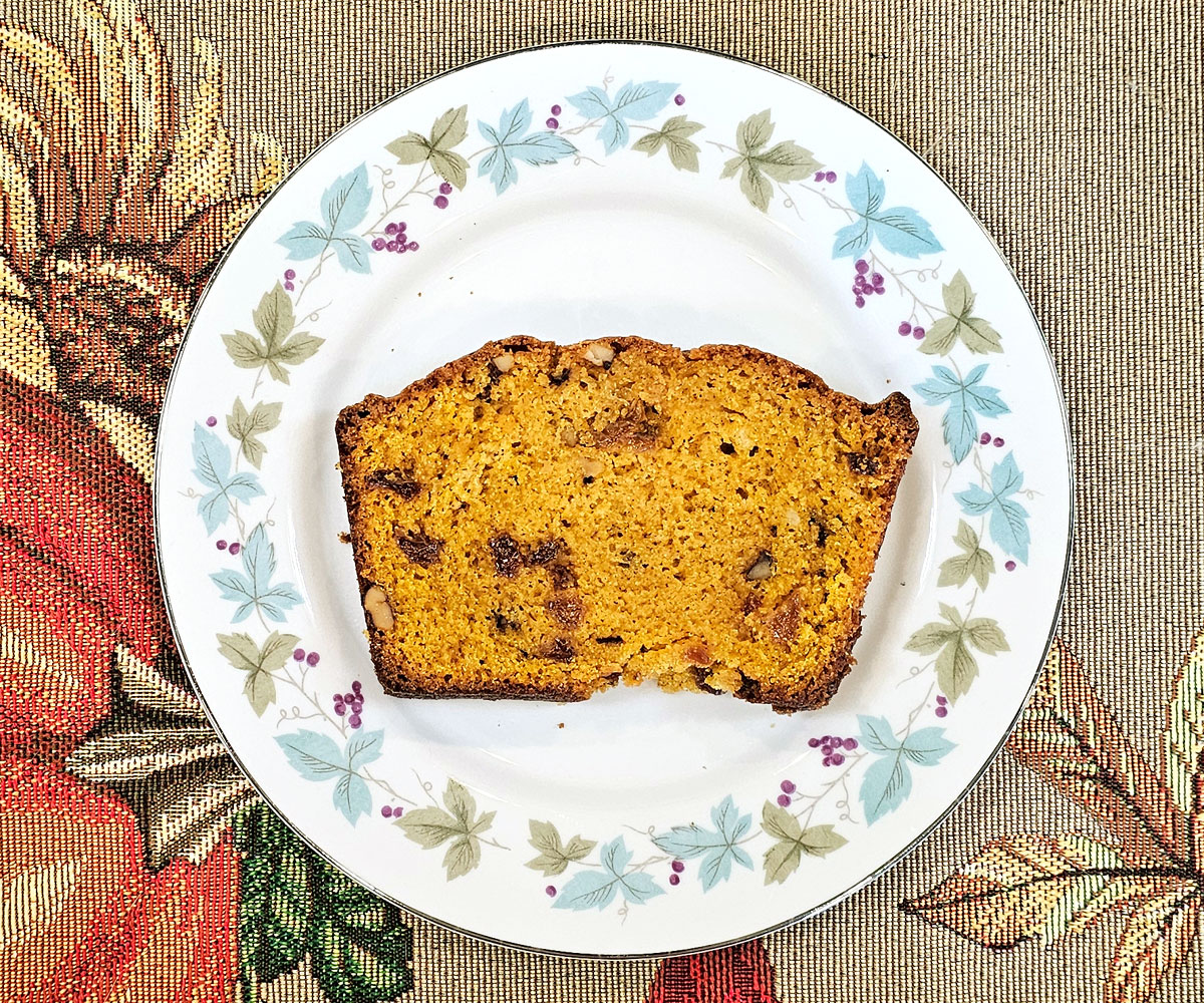 plate with a slice of butternut squash bread on it, sitting on a decorative autumn table runner.