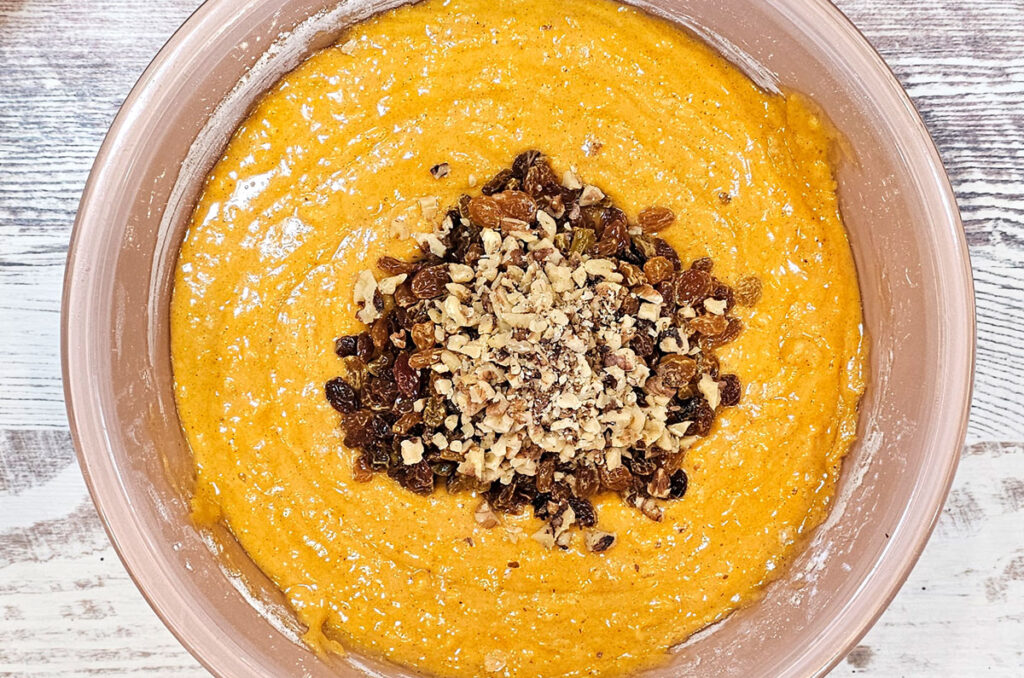 Large mixing bowl with all the ingredients stirred together except nuts and raisins floating on top, ready to be stirred in.