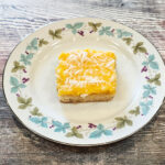 A piece of tropical papaya lemon bar on a round plate on a countertop.